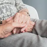 Dłonie opiekuna obejmują dłoń osoby starszej, symbolizując troskę i wsparcie. To codzienne obowiązki opiekuna osoby niepełnosprawnej.