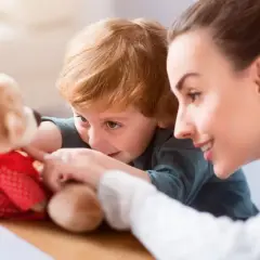 Uśmiechnięta opiekunka dziecięca praca z chłopcem i pluszowym misiem.