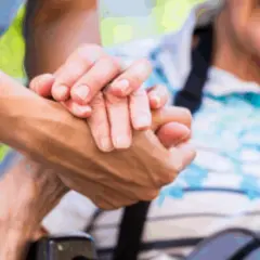 Dłoń opiekunki obejmuje dłoń starszej osoby, symbolizując troskę i wsparcie przy zatrudnieniu opiekunki przez osobę prywatną.