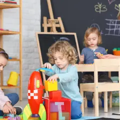 Dzieci bawią się klockami w żłobku, a opiekunka czuwa nad ich bezpieczeństwem. Zastanawiasz się, ile zarabia opiekunka w żłobku?
