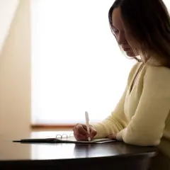 Opiekunka dziecięca pisze w wypełnionym dzienniku praktyk, notując ważne wydarzenia dnia.