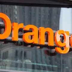 Pomarańczowe litery "Orange" na budynku. Firma ta oferuje usługi telekomunikacyjne, a jej nazwa kojarzy się z dobrymi zarobkami.