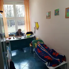 Pielęgniarka szkolna przygotowuje materiały do kursu online, podczas gdy dziecko odpoczywa pod kocem.
