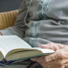 Dłonie seniora trzymają otwartą książkę. Czytanie to świetne pomysły na zajęcia z seniorami, rozwijające wyobraźnię i wiedzę.