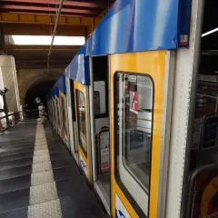 Żółto-niebieski wagonik metra neapol stoi na peronie, obok schodów prowadzących do tunelu.