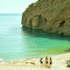 Trzy dziewczyny idą plażą w Grecji, gdzie woda jest turkusowa, a klify imponujące. Czy w Grecji jest drogo? Widok sugeruje, że można tu znaleźć rajskie zakątki.