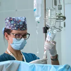 Pielęgniarka oddziałowa w maseczce i czepku z gwiazdkami przygotowuje kroplówkę. Ciekawe, ile zarabia pielęgniarka oddziałowa za taką odpowiedzialną pracę.