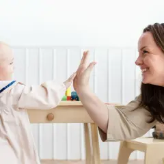 Uśmiechnięty opiekun w żłobku daje piątkę dziecku przy stoliku z zabawkami.