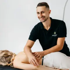 Uśmiechnięty masażysta wykonuje masaż klasyczny pleców. Uczy się technik na kursie masażu.