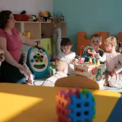 Jedna opiekunka w żłobku dogląda kilkorga dzieci bawiących się zabawkami.