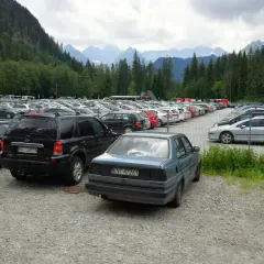 Duży tatrzańska łomnica parking pełen samochodów, zalesione zbocza i góry w tle.