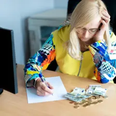 Zmartwiona kobieta z notatkami i pieniędzmi na biurku, analizująca ceny na Białorusi.
