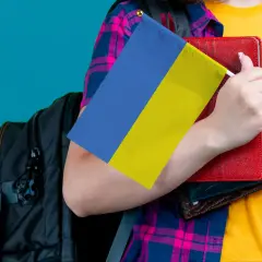 Osoba z plecakiem trzyma flagę Ukrainy i książki. Ceny we Lwowie mogą być różne, ale wiedza jest bezcenna.