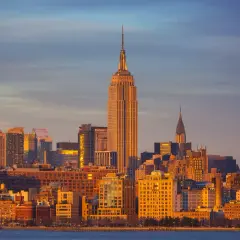 Zachód słońca nad Manhattanem. Widać Empire State Building i Chrysler Building. Zastanawiasz się, ile się leci do Nowego Jorku?