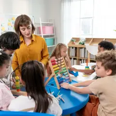 Nauczycielka podczas kursu opiekunki dziecięcej w przedszkolu pomaga dzieciom w zabawie z liczydłem i innymi zabawkami edukacyjnymi.
