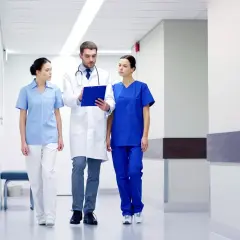 Lekarz i dwie pielęgniarki idą korytarzem szpitalnym, dyskutując o pracy. Zastanawiasz się nad asystent medyczny zarobki?