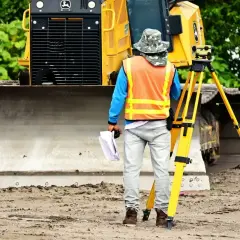 Geodeta w kamizelce odblaskowej z niwelatorem i dokumentami. Zastanawia się, ile zarabia technik na budowie.