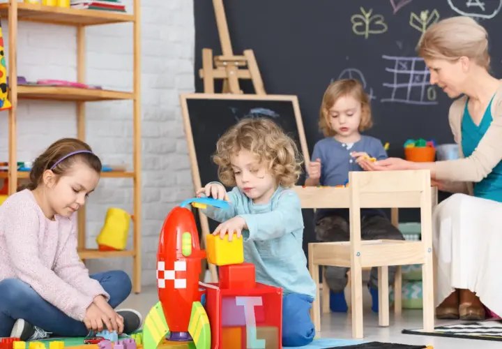 Dzieci bawią się klockami w żłobku, a opiekunka czuwa nad ich bezpieczeństwem. Zastanawiasz się, ile zarabia opiekunka w żłobku?