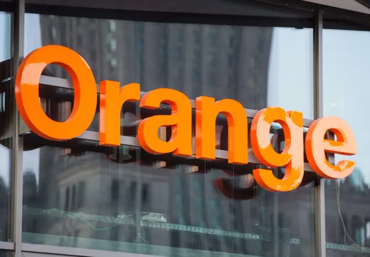 Pomarańczowe litery "Orange" na budynku. Firma ta oferuje usługi telekomunikacyjne, a jej nazwa kojarzy się z dobrymi zarobkami.