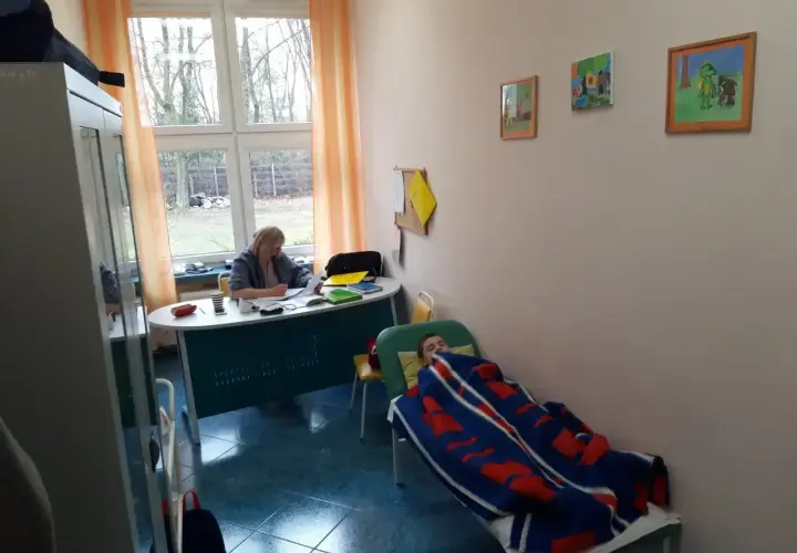 Pielęgniarka szkolna przygotowuje materiały do kursu online, podczas gdy dziecko odpoczywa pod kocem.