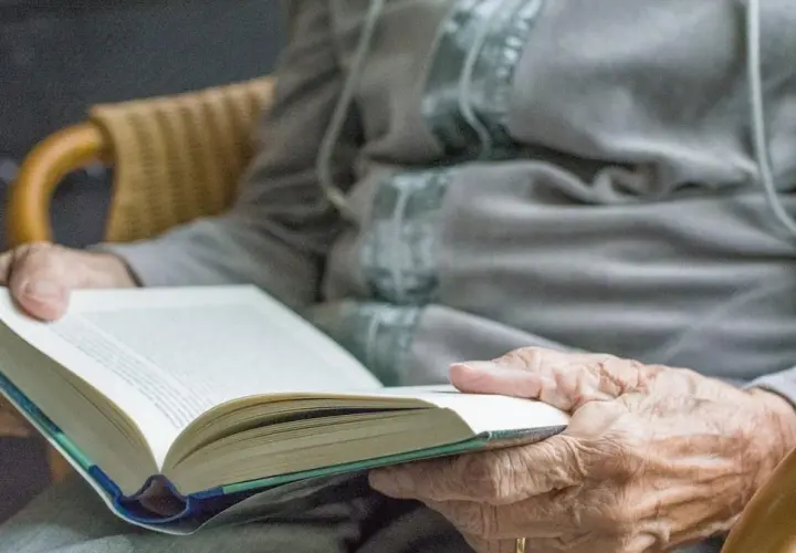 Dłonie seniora trzymają otwartą książkę. Czytanie to świetne pomysły na zajęcia z seniorami, rozwijające wyobraźnię i wiedzę.