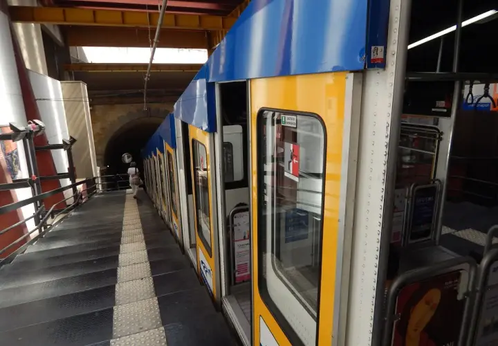 Żółto-niebieski wagonik metra neapol stoi na peronie, obok schodów prowadzących do tunelu.