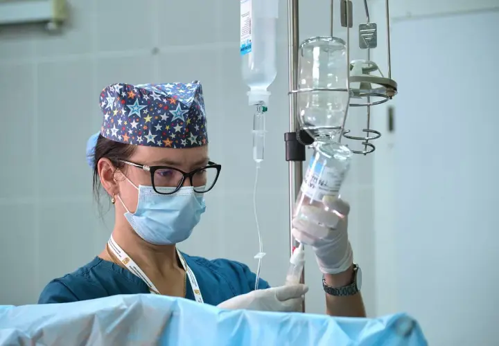 Pielęgniarka oddziałowa w maseczce i czepku z gwiazdkami przygotowuje kroplówkę. Ciekawe, ile zarabia pielęgniarka oddziałowa za taką odpowiedzialną pracę.