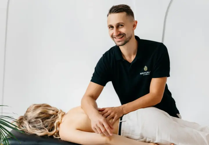 Uśmiechnięty masażysta wykonuje masaż klasyczny pleców. Uczy się technik na kursie masażu.