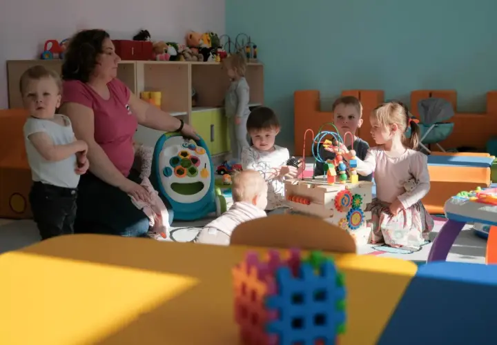Jedna opiekunka w żłobku dogląda kilkorga dzieci bawiących się zabawkami.