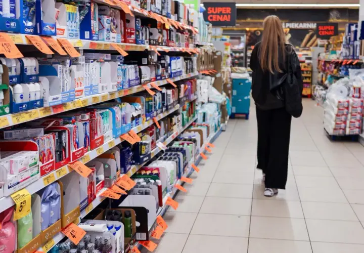 Kobieta spaceruje między regałami pełnymi produktów w sklepach w Czechach. Widać pasty do zębów, kosmetyki i inne artykuły.
