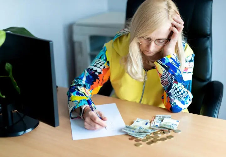 Zmartwiona kobieta z notatkami i pieniędzmi na biurku, analizująca ceny na Białorusi.