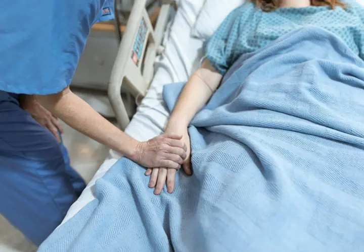 Opiekunka trzyma za rękę pacjentkę w hospicjum dla osób starszych. Ciepło i troska w tym trudnym miejscu.