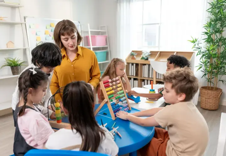 Nauczycielka podczas kursu opiekunki dziecięcej w przedszkolu pomaga dzieciom w zabawie z liczydłem i innymi zabawkami edukacyjnymi.