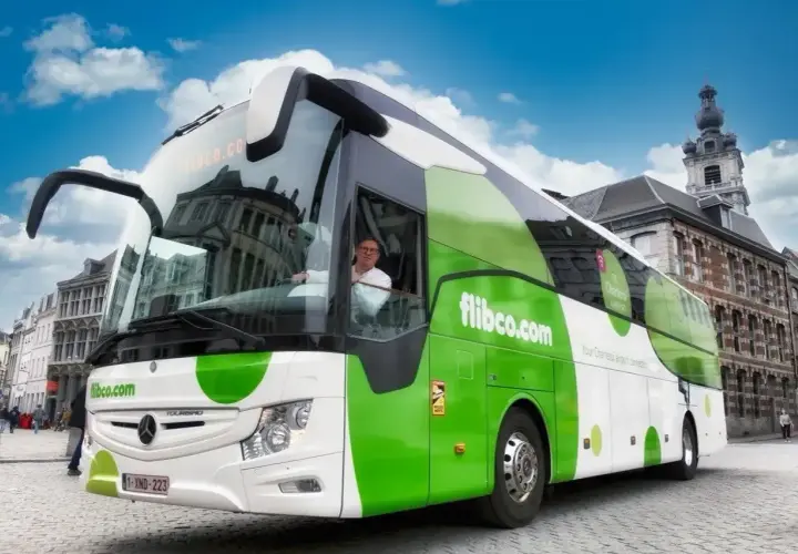 Zielony autokar flibco.com na brukowanej ulicy w Brukseli. Kierowca w okularach pozdrawia.