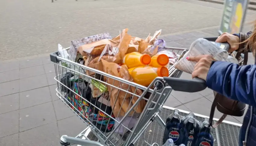 Pełny wózek zakupowy, w tym napoje i produkty spożywcze, sugeruje analizę cen w Wilnie.
