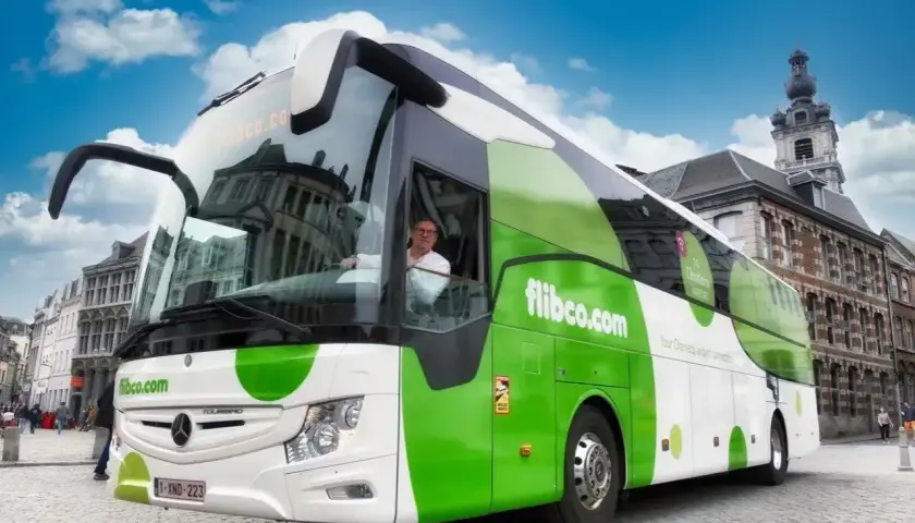 Zielony autokar flibco.com na brukowanej ulicy w Brukseli. Kierowca w okularach pozdrawia.