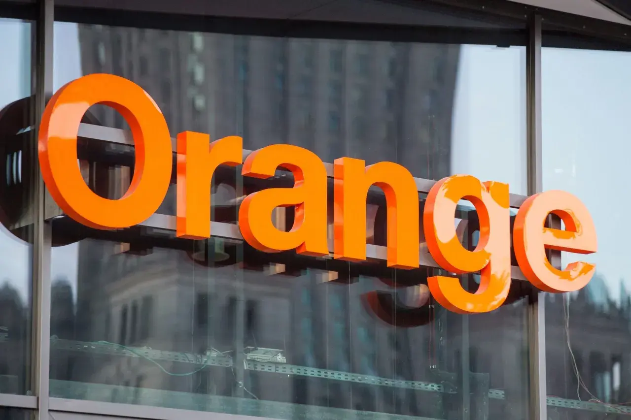 Pomarańczowe litery "Orange" na budynku. Firma ta oferuje usługi telekomunikacyjne, a jej nazwa kojarzy się z dobrymi zarobkami.