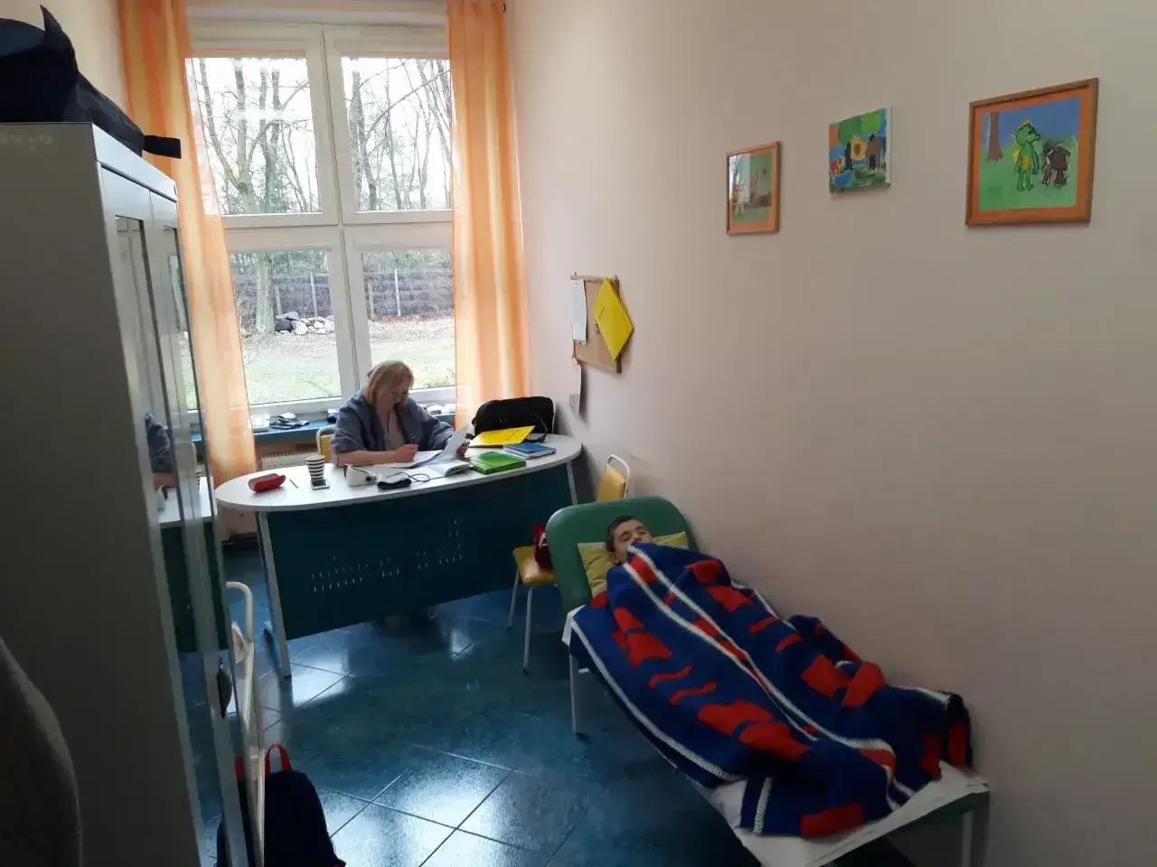 Pielęgniarka szkolna przygotowuje materiały do kursu online, podczas gdy dziecko odpoczywa pod kocem.