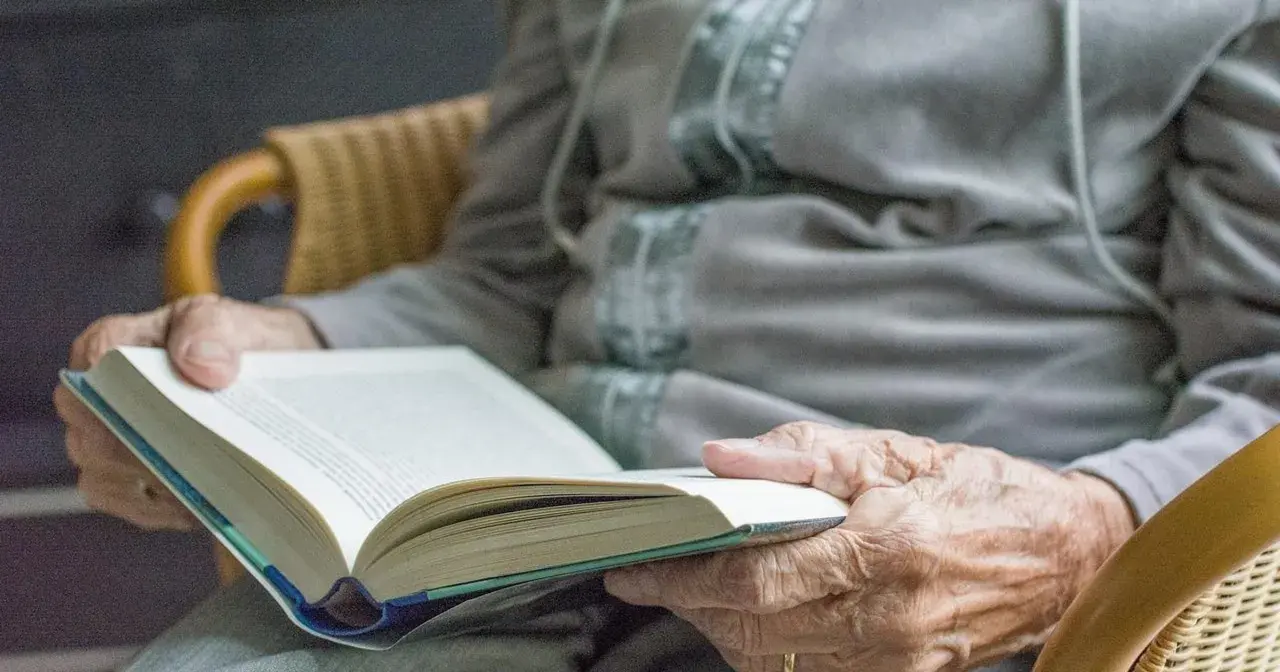 Dłonie seniora trzymają otwartą książkę. Czytanie to świetne pomysły na zajęcia z seniorami, rozwijające wyobraźnię i wiedzę.