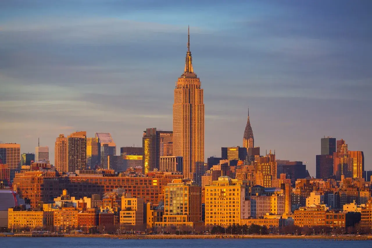 Zachód słońca nad Manhattanem. Widać Empire State Building i Chrysler Building. Zastanawiasz się, ile się leci do Nowego Jorku?