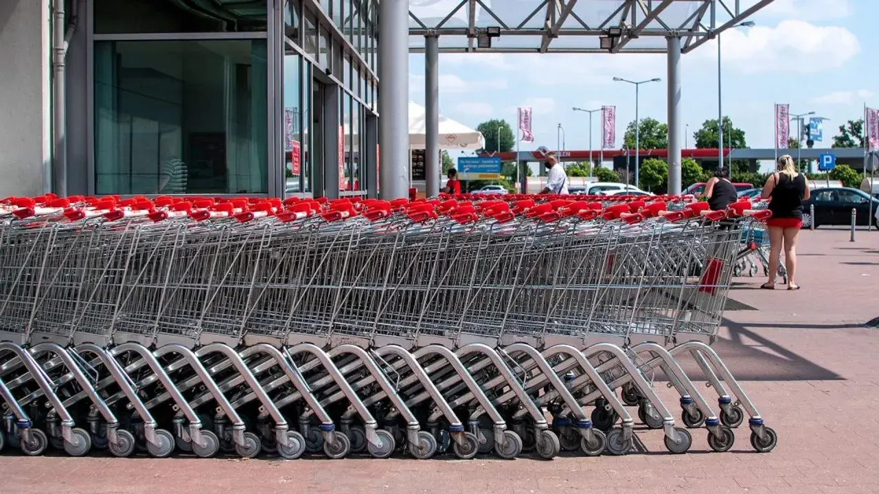 Rzędy wózków sklepowych z czerwonymi uchwytami przed francuskim hipermarketem.