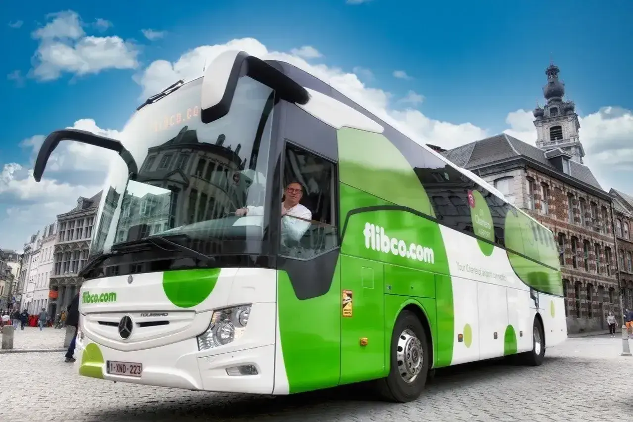 Zielony autokar flibco.com na brukowanej ulicy w Brukseli. Kierowca w okularach pozdrawia.