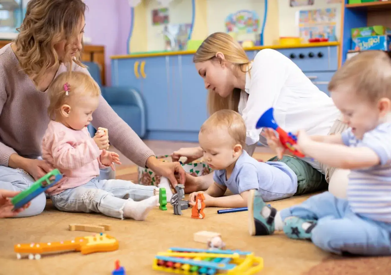 Dwie opiekunki bawią się z dziećmi w żłobku. Widać, ile opiekunek w żłobku jest potrzebnych, by zapewnić maluchom bezpieczeństwo i radość.