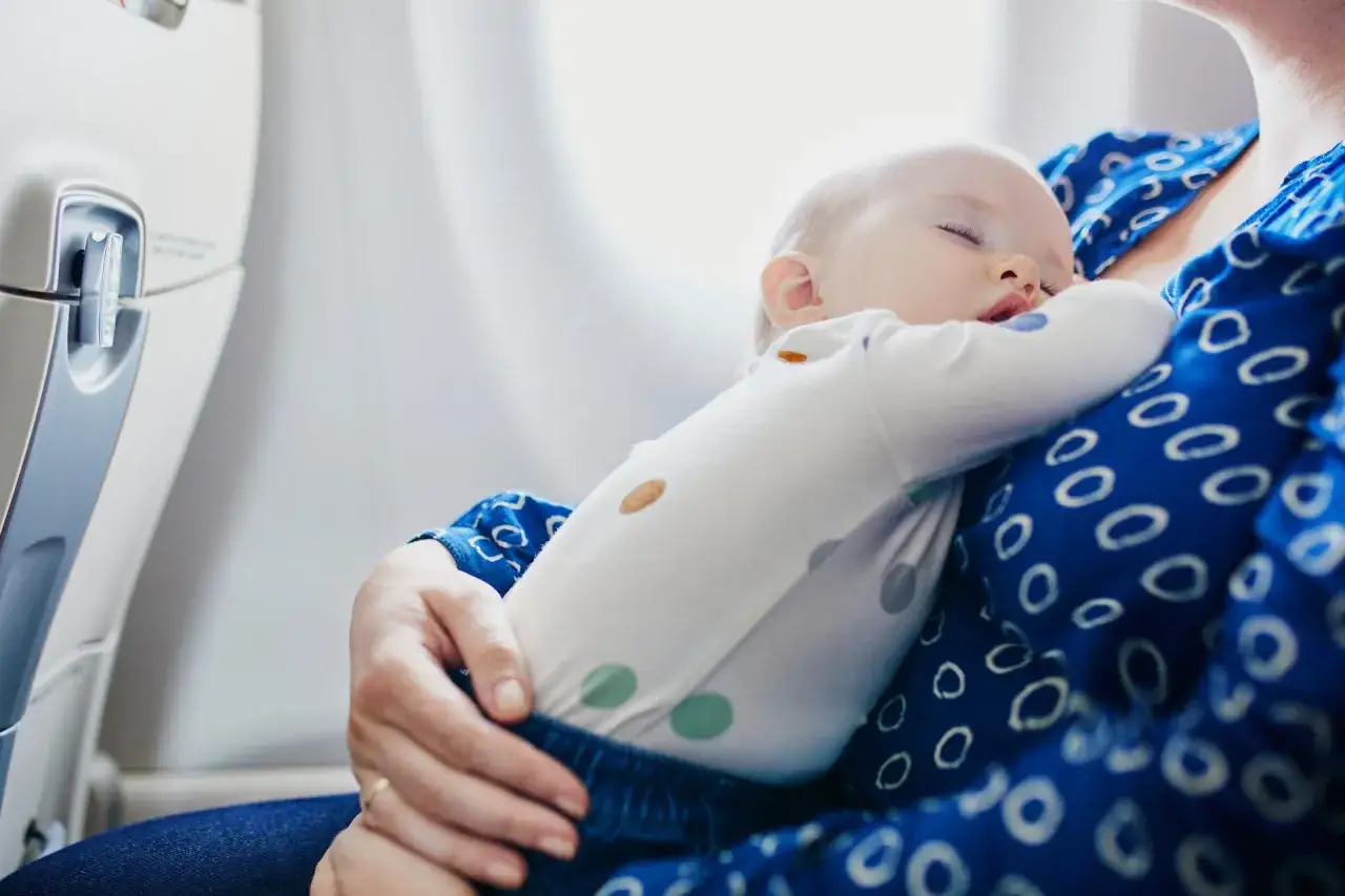 Śpiące dziecko na rękach mamy w samolocie. To bagaż dla niemowlaka, kt&oacute;ry podr&oacute;żuje z rodzicami.