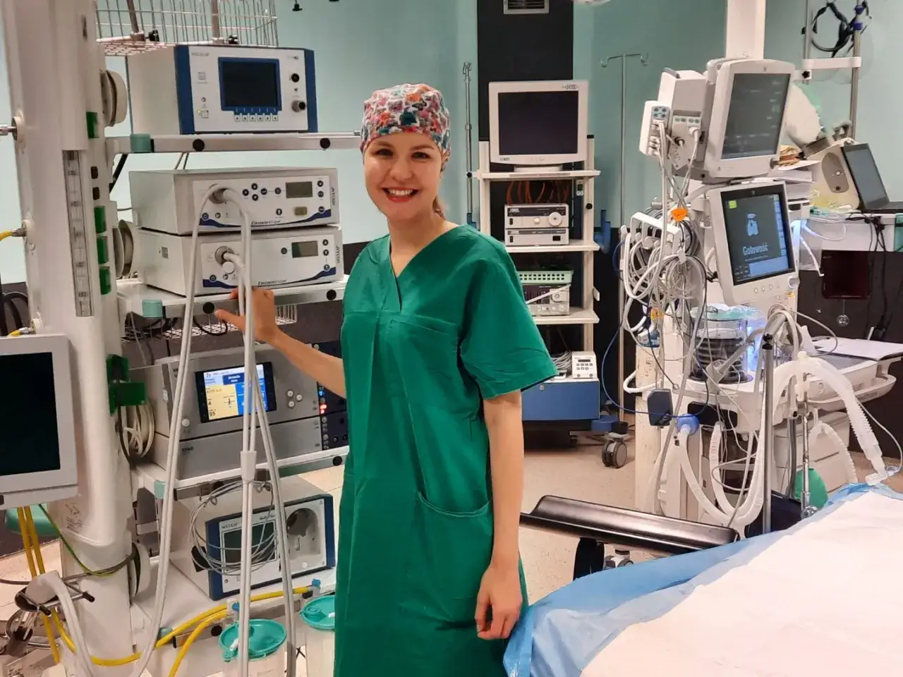 Uśmiechnięta instrumentariuszka na kursie, otoczona aparaturą medyczną na sali operacyjnej.