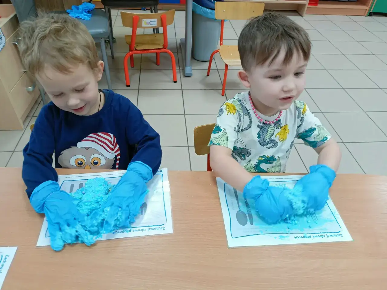 Dw&oacute;ch chłopc&oacute;w w niebieskich rękawiczkach bawi się niebieską masą sensoryczną. To wesołe zabawy w żłobku dla rocznych dzieci, rozwijające zmysły.