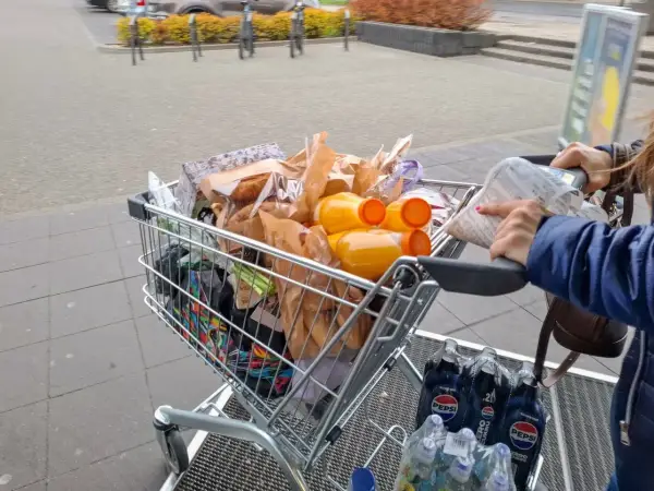 Pełny wózek zakupowy, w tym napoje i produkty spożywcze, sugeruje analizę cen w Wilnie.